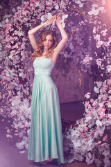 Fototapeta premium Beautiful woman model in a mint-colored dress on a flowered spring background. Beauty girl with a stunning makeup and hairstyle.
