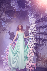 Fototapeta premium Beautiful woman model in a mint-colored dress on a flowered spring background. Beauty girl with a stunning makeup and hairstyle.