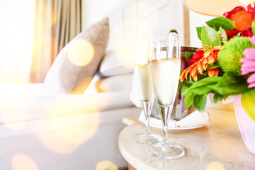 Two glasses of champagne in the upscale hotel room. Dating, romance, honeymoon, valentine, getaway concepts. Horizontal, light festive bokeh lights