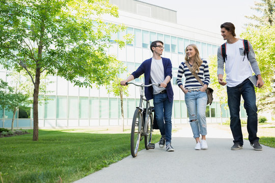 College students with bicycle walking on campus sidewalk