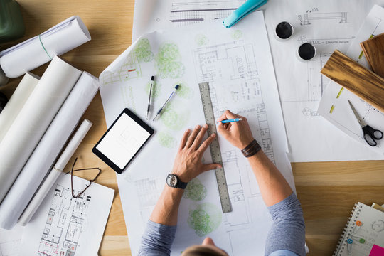 Overhead View Architect Drafting Blueprints At Table