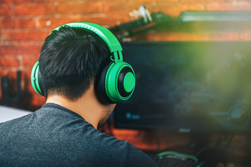 Back view of gamer in green professional headphones using computer for playing game.