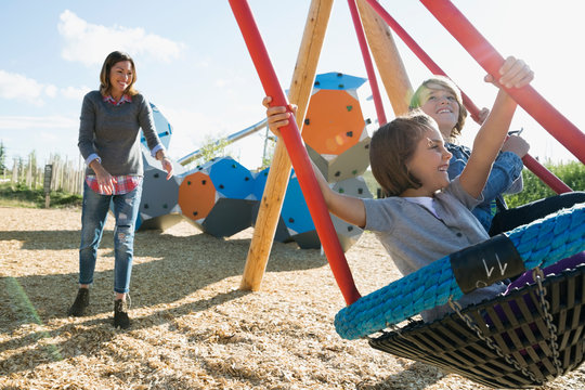 Mother pushing daughter and son in playground swing