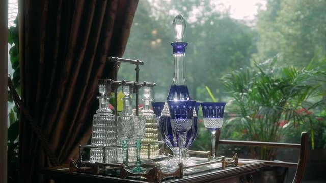 Beautiful crystal decanters with alcohol stand on a table near a window with greens