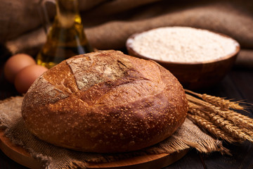 Loaf of bread on a wooden background, food closeup. Against the background of flour and vegetable oil with eggs.