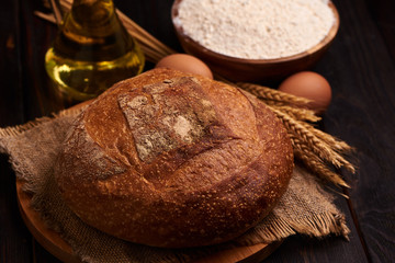 Loaf of bread on a wooden background, food closeup. Against the background of flour and vegetable oil with eggs.