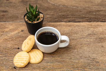 A white cup of coffee with cookie on the wooden table background.