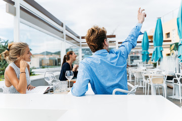 guy asking the waiter at an outdoor restaurant during a date with a young girl