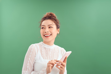 Cheerful happy young Asian woman using smartphone isolated over green background.