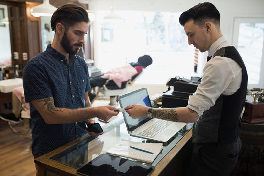 Man Paying Barber At Counter In Barber Shop