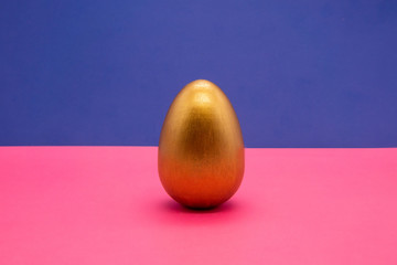 one gold Easter eggs on blue and pink background