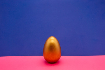 one gold Easter eggs on blue and pink background