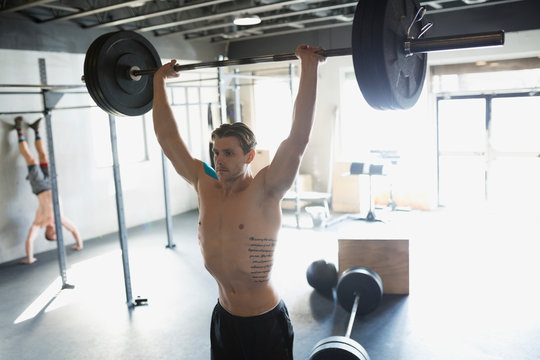 Tattooed Man Weightlifting Barbell Overhead At Gym