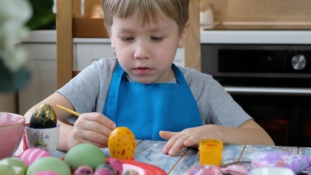 Five years old child boy kid coloring easter eggs in the kitchen.