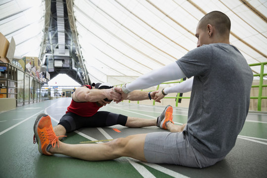 Runners Holding Hands Stretching Legs Apart Indoor Track