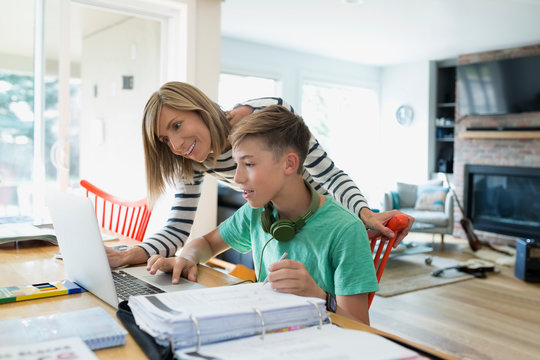 Mother helping son doing homework at dining table