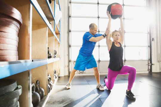 Gym Instructor Assisting Woman With Medicine Ball Lunge