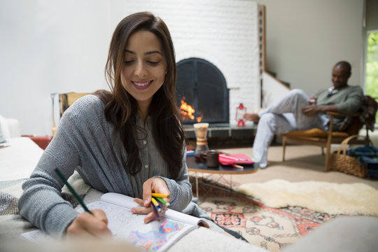 Smiling woman coloring in coloring book in living room near fireplace