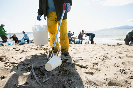 Beach cleanup volunteer using claw to pick up litter on beach