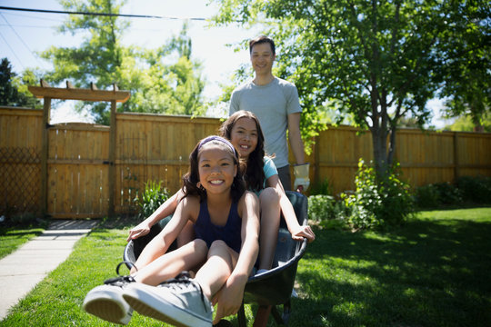 Portrait smiling father pushing daughters in wheelbarrow in sunny backyard
