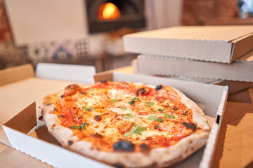 Pizza delivery concept. Baked products in a cardboard box against a wooden background. Baked tasty margherita pizza in Traditional wood oven in Neapolitan restaurant, Italy.
