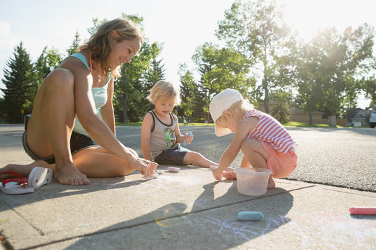 Family drawing with sidewalk chalk on sunny sidewalk