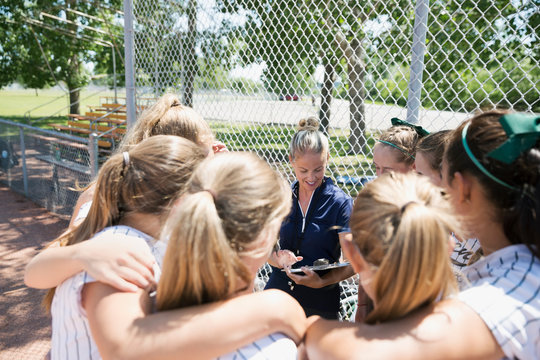 Coach And Middle School Girl Softball Team In Huddle On Baseball Diamond