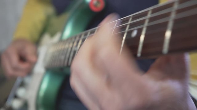 A close-up of a guitar master's hand sliding on the neck playing chords, scales and solos on a metallic green vintage electric guitar