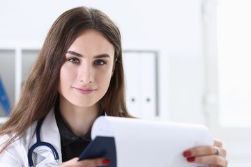 Beautiful smiling female doctor hold clipboard pad and fill something with silver pen. Physical illness prevention prescribe remedy ward round therapeutist assistance healthy lifestyle concept