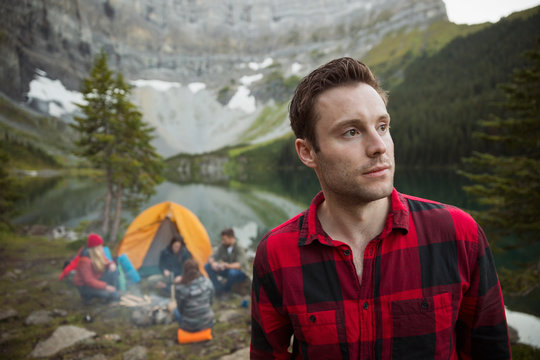 Pensive man looking away at remote lakeside campsite