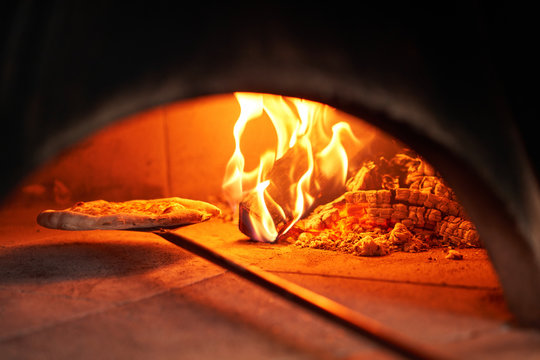 Baked tasty margherita pizza in Traditional wood oven in Naples restaurant, Italy. Original neapolitan pizza. Red hot coal.