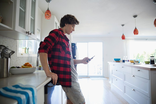 Young man texting with cell phone in kitchen