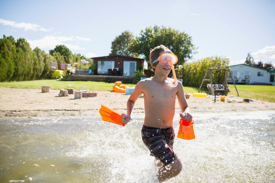 Boy With Snorkel And Flippers Running In Sunny Summer Lake