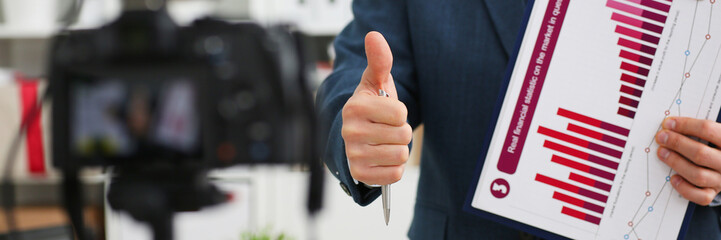 Male in suit and tie show confirm sign arm making promo videoblog or photo session in office camcorder to tripod closeup. Vlogger promotion selfie solution or finance advisor management information © H_Ko