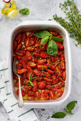 Baked cherry tomato with garlic, thyme and basil in old baking pan on concrete vintage background. Top view.