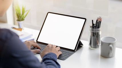 Cropped shot of professional businessman typing on blank screen tablet and office supplies