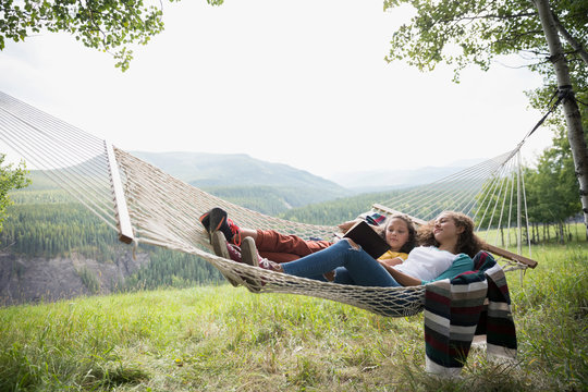 Sisters laying in rural hammock reading book