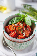 Baked cherry tomato with garlic, thyme and basil in vintage ceramic bowls on a light wooden table. Top view.