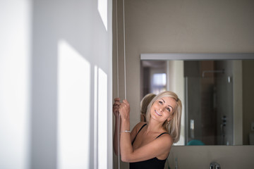Fototapeta na wymiar Pretty, young woman lowering the interior shades/blinds in her modern interior apartment