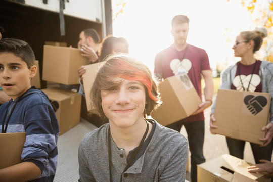 Portrait smiling tween boy volunteering helping unload cardboard boxes from truck