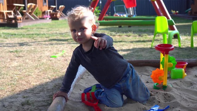 Blond little child boy play in sandbox at playground.