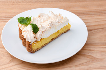 Lemon meringue pie. Lemon tart on a white plate with a mint leaf on light wooden table.