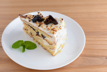 Vanilla sponge cake biscuit with prune, walnuts and frosting served on a white plate, on light wooden background table