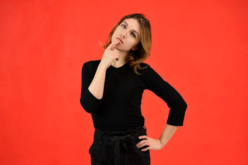 A universal concept, the picture is suitable for any topic. Studio portrait of a pretty blonde girl in a black T-shirt on a red background with bright emotions.