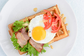 Classic eggs and bacon meat on waffles breakfast with tomatoes and salad served on a white plate on white background