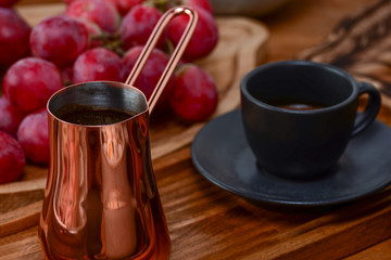 Turkish coffee in traditional embossed metal cup cezve. Georgian coffe in black cup with grapes on dark wooden table