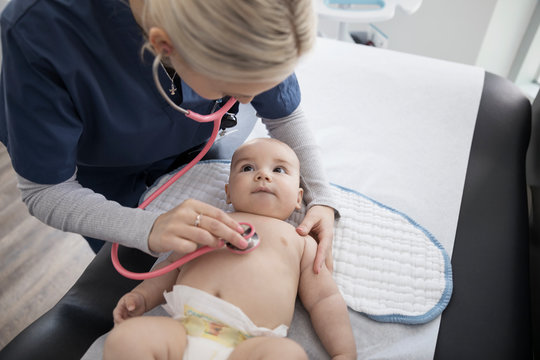 Female nurse with stethoscope examining baby boy in medical examination room
