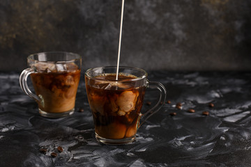  Two transparent cups of cold coffee with milk. Iced coffee.Stream of milk. Copy space. Close up. Milk explosion in iced coffee.