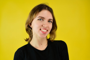 Close-up Studio portrait of a pretty blonde girl in a black T-shirt on a yellow background with bright emotions. A universal concept, the picture is suitable for any topic.