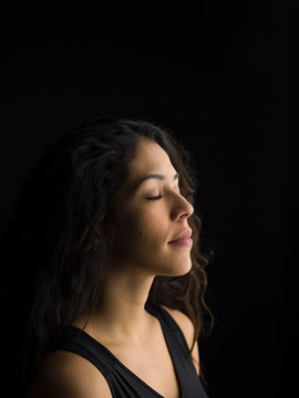 Portrait serene Latina woman with eyes closed and long black hair against black background